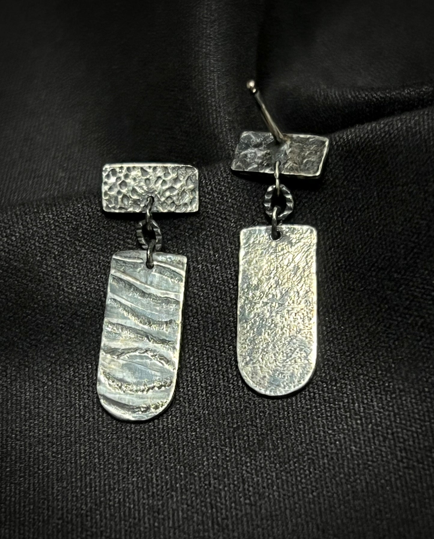 Pair of silver earrings on a black fabric background